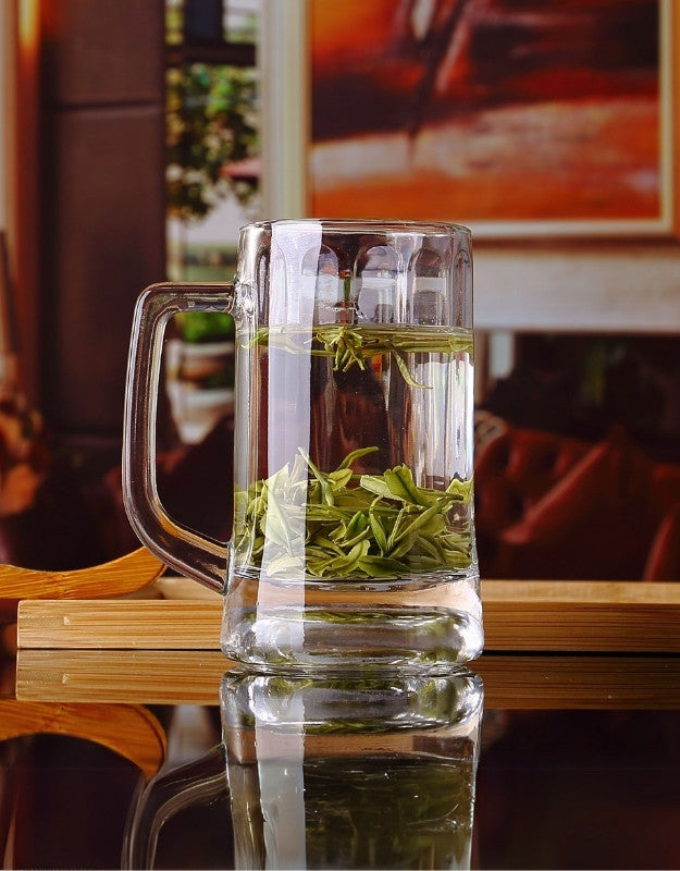 Clear glass mug with green tea leaves on a reflective surface. Clear glass beer mug filled with green tea leaves and hot water on a reflective table.